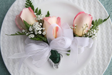 Pink rose boutonniere with greenery and white ribbon, elegant floral accessory for prom or formal event.